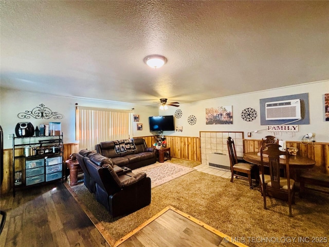 living room with ceiling fan, a wainscoted wall, a textured ceiling, and a wall unit AC