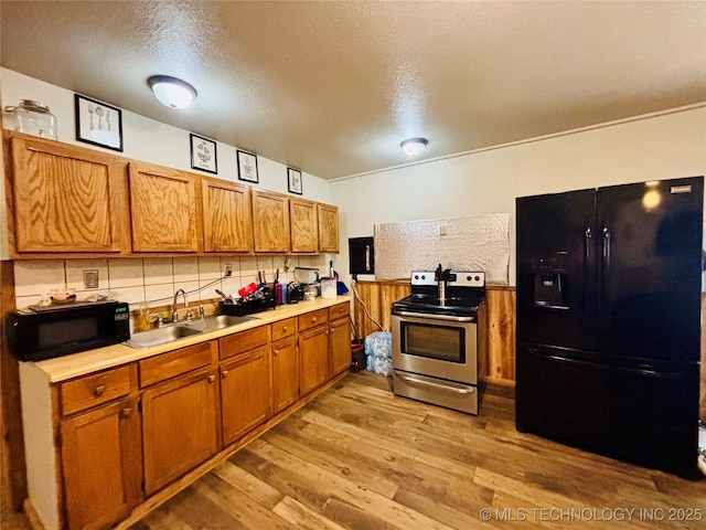 kitchen with brown cabinets, light countertops, a sink, black appliances, and light wood-style flooring