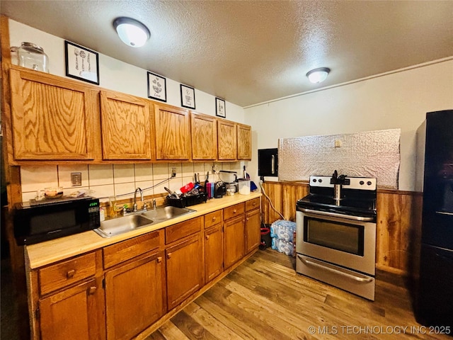 kitchen with light countertops, wood finished floors, a sink, black appliances, and a textured ceiling