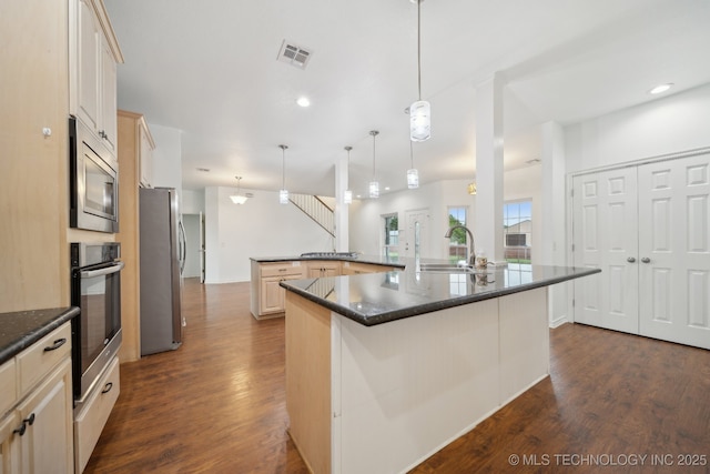 kitchen with visible vents, appliances with stainless steel finishes, a large island with sink, a sink, and dark wood-type flooring