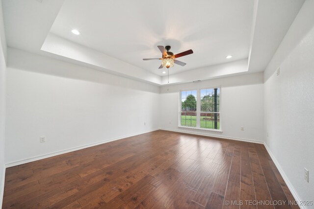 spare room with a raised ceiling, ceiling fan, baseboards, and dark wood finished floors