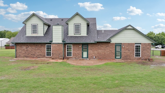 rear view of property featuring roof with shingles, a patio area, brick siding, fence, and a yard