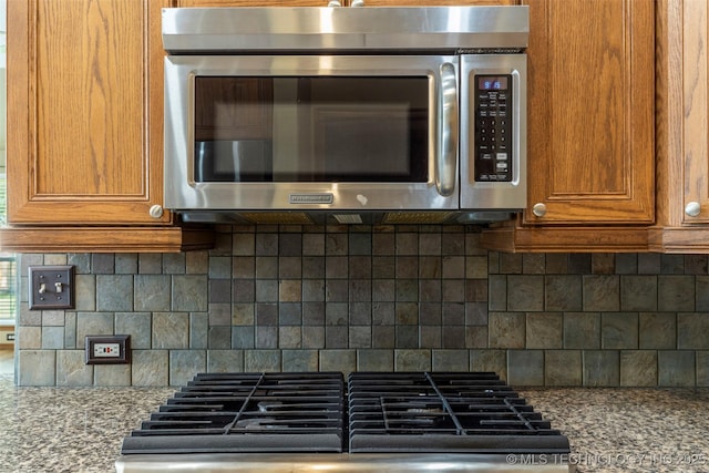 3701 Bridgeport Rd, Norman, OK 73072 - kitchen with stainless steel microwave, brown cabinets, tasteful backsplash, and light stone countertops