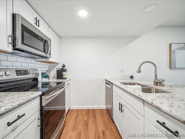 kitchen featuring stainless steel appliances, a sink, light wood-style floors, tasteful backsplash, and white cabinetry