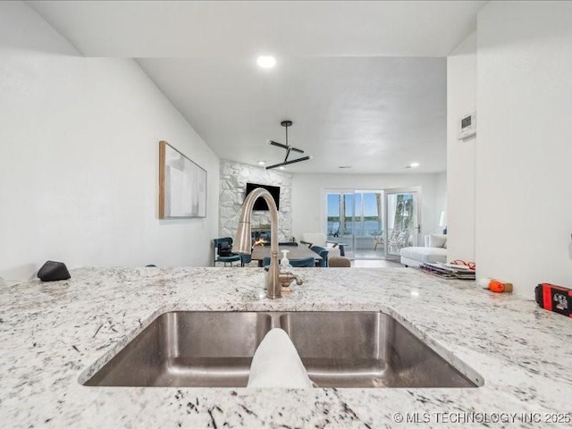 kitchen with recessed lighting, open floor plan, light stone counters, and a sink