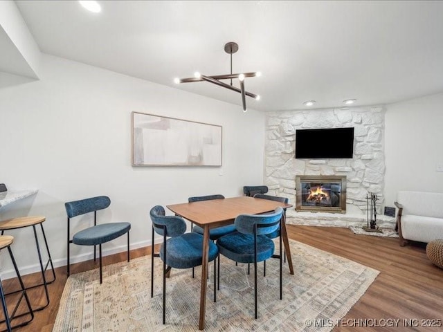 dining area with wood finished floors, an inviting chandelier, a fireplace, baseboards, and recessed lighting