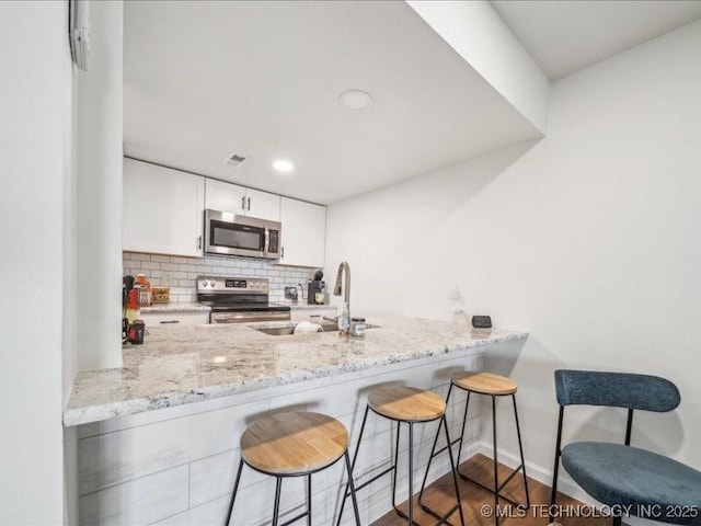 kitchen featuring white cabinets, a sink, a peninsula, appliances with stainless steel finishes, and a breakfast bar area