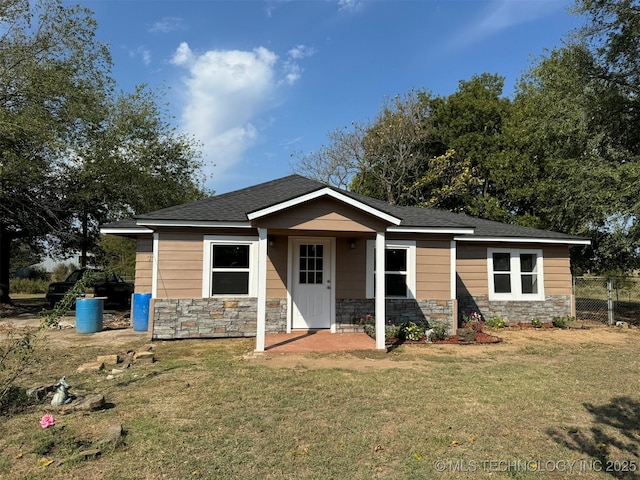 bungalow-style house featuring a shingled roof, fence, a front lawn, and stone siding