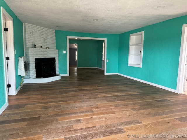unfurnished living room with a fireplace, a textured ceiling, wood finished floors, and baseboards