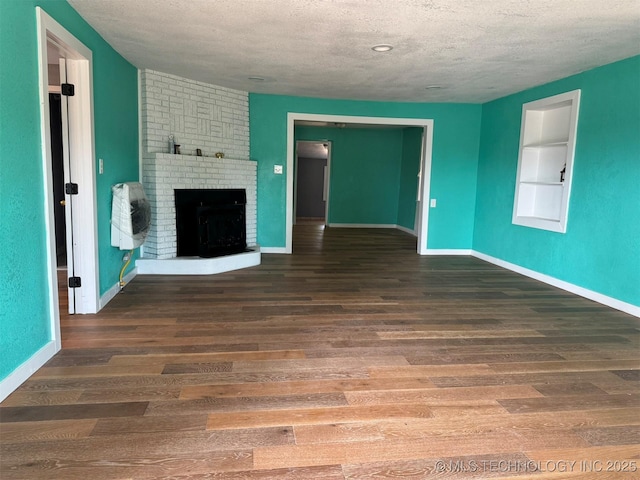 unfurnished living room featuring a brick fireplace, a textured ceiling, wood finished floors, and baseboards