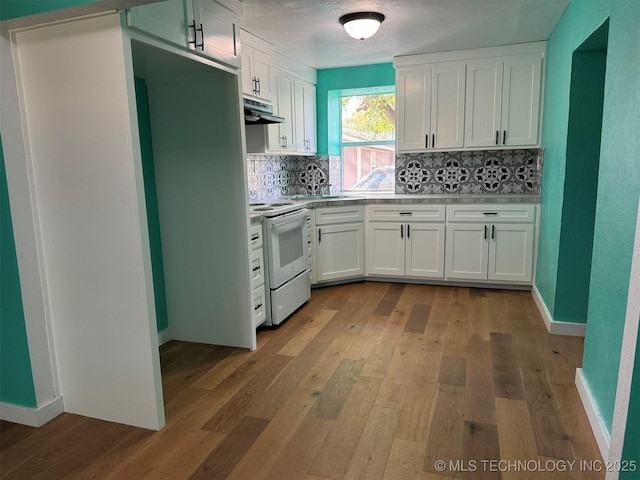 kitchen with white electric stove, light wood-style floors, under cabinet range hood, backsplash, and white cabinetry