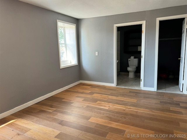 unfurnished bedroom featuring baseboards, a spacious closet, connected bathroom, and light wood-style floors