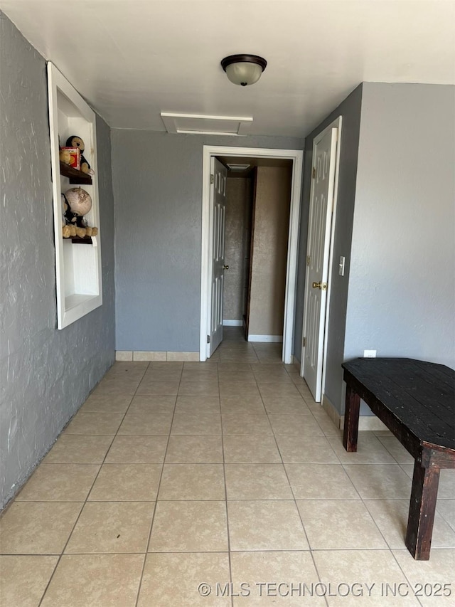 corridor with attic access, tile patterned flooring, and a textured wall