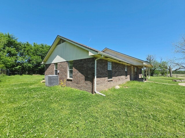 view of side of home featuring brick siding, a yard, and central air condition unit