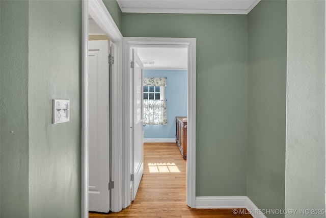 corridor featuring light wood-style flooring, baseboards, and crown molding
