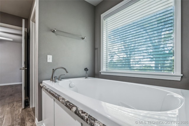 full bathroom with a bath, plenty of natural light, baseboards, and wood finished floors