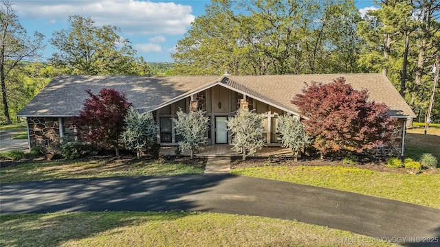 view of front of home with a front lawn, stone siding, a shingled roof, and covered porch