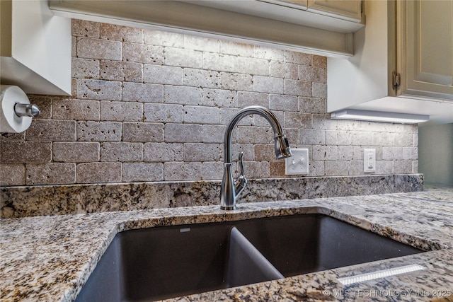 details featuring a sink, light stone counters, and tasteful backsplash