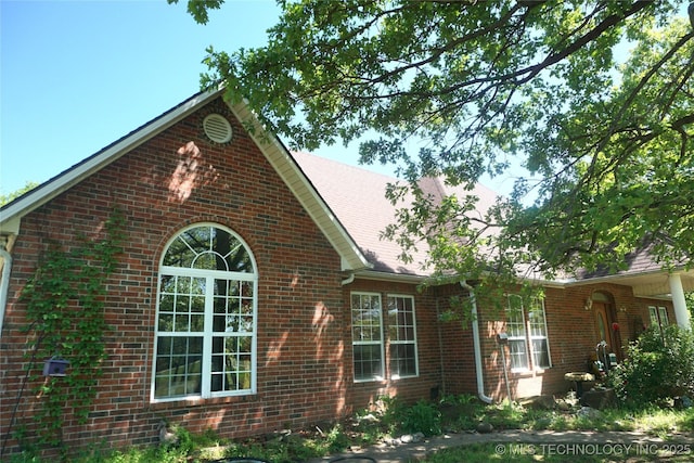 view of property exterior featuring brick siding and a shingled roof