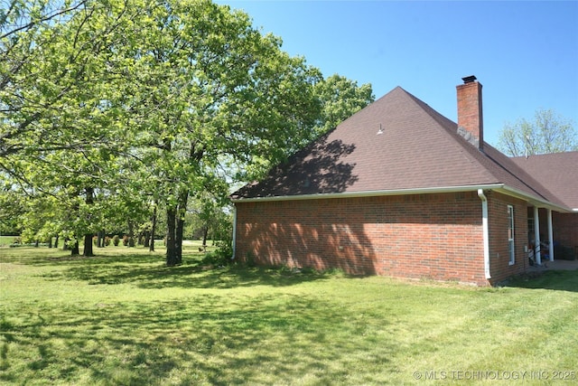 view of home's exterior featuring brick siding, a lawn, a chimney, and roof with shingles