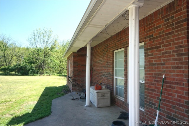 view of side of home with a patio area, a lawn, and brick siding