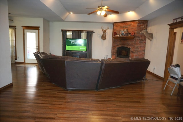 living room with a tray ceiling, wood finished floors, baseboards, a fireplace, and ceiling fan