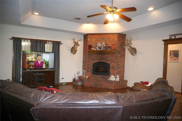 living room with a tray ceiling, wood finished floors, visible vents, and ceiling fan