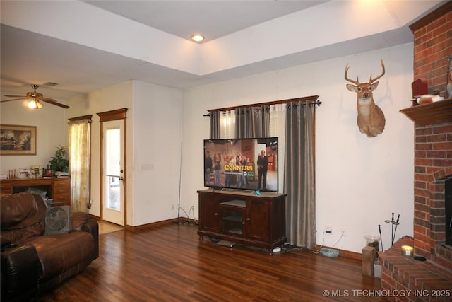 living room featuring wood finished floors, visible vents, baseboards, a fireplace, and ceiling fan
