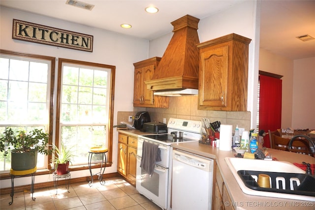 kitchen with a sink, visible vents, custom exhaust hood, decorative backsplash, and white appliances
