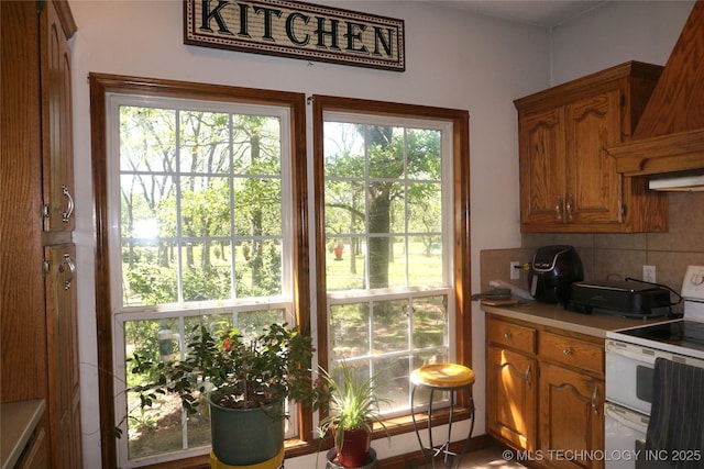 kitchen featuring white electric stove, light countertops, decorative backsplash, brown cabinetry, and custom range hood
