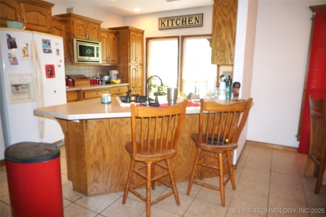 kitchen featuring a kitchen breakfast bar, backsplash, a sink, stainless steel microwave, and white refrigerator with ice dispenser