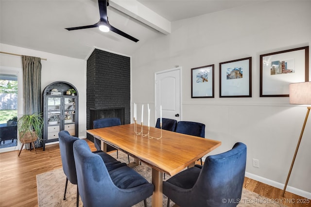 dining space featuring lofted ceiling with beams, wood finished floors, a fireplace, and ceiling fan