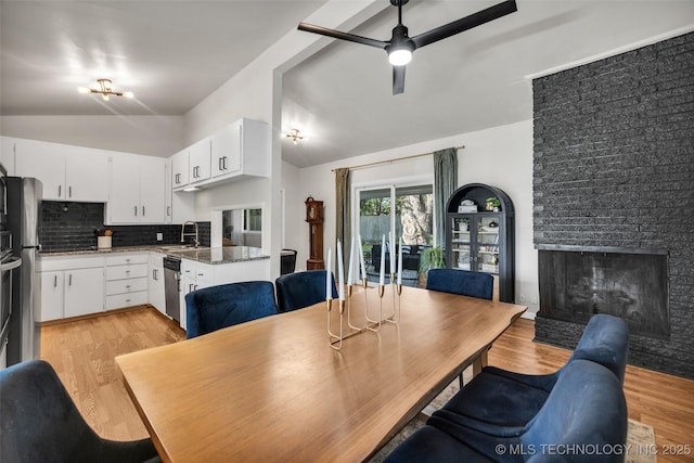 dining room with a fireplace, vaulted ceiling, light wood finished floors, and ceiling fan