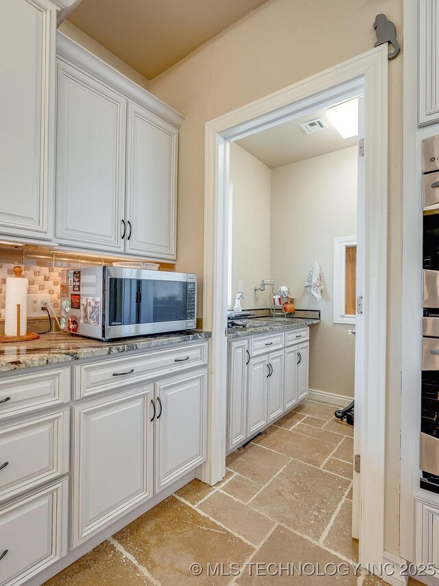 21125 State Highway 99 S, Stonewall, OK 74871 - kitchen with stone tile floors, stainless steel microwave, backsplash, white cabinetry, and visible vents