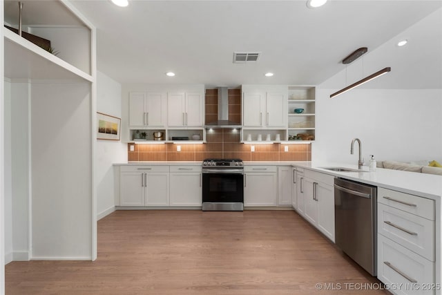 kitchen with stainless steel appliances, open shelves, wall chimney range hood, visible vents, and a sink