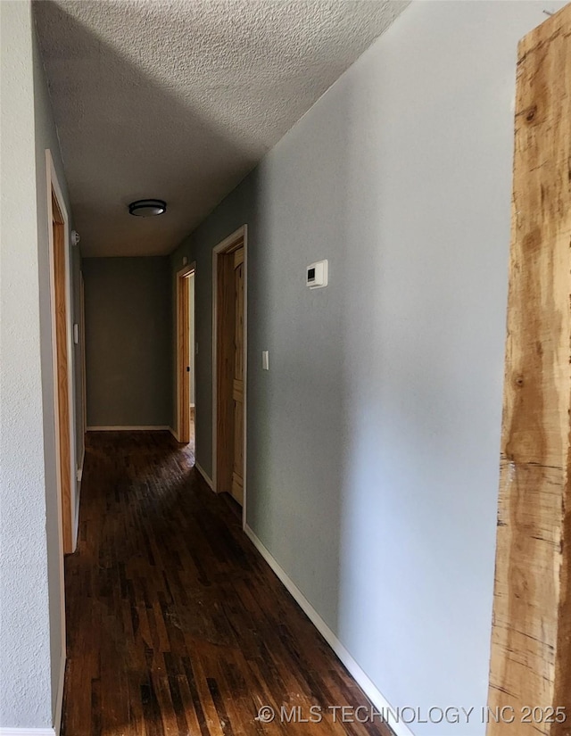 hallway featuring wood finished floors, a textured ceiling, and baseboards