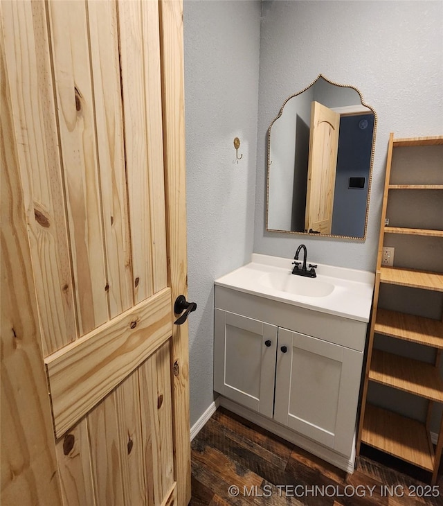 bathroom with baseboards, wood finished floors, vanity, and a textured wall