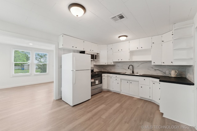 kitchen with a sink, open shelves, light wood-type flooring, dark countertops, and appliances with stainless steel finishes