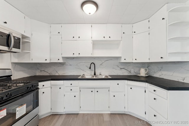kitchen featuring white cabinetry, open shelves, a sink, appliances with stainless steel finishes, and dark countertops