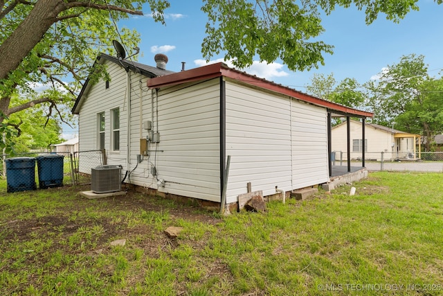 view of side of home with a lawn, central AC, and fence