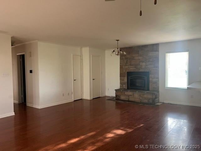 unfurnished living room featuring baseboards, a notable chandelier, wood finished floors, and a fireplace
