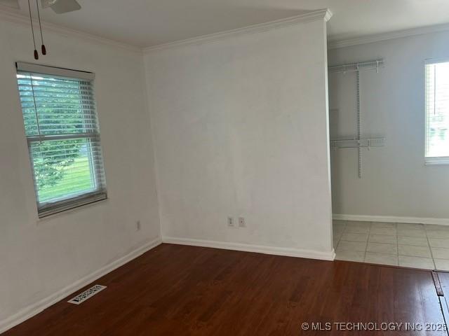 unfurnished room with ceiling fan, visible vents, wood finished floors, baseboards, and ornamental molding