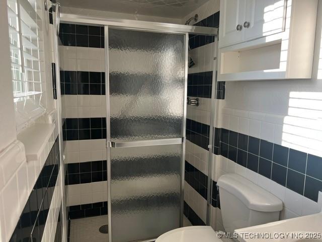 full bathroom with a stall shower, a healthy amount of sunlight, toilet, and tile walls