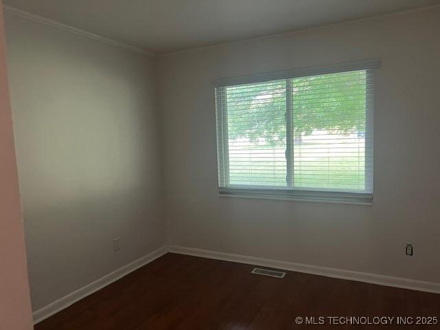 unfurnished room featuring baseboards, ornamental molding, dark wood-style flooring, and visible vents
