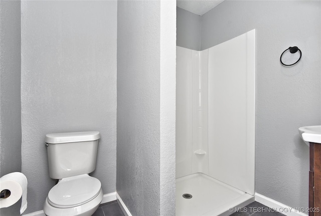 bathroom with vanity, a textured wall, toilet, baseboards, and a shower stall