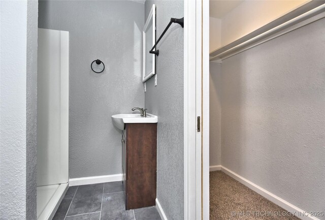 bathroom with tile patterned flooring, a textured wall, a spacious closet, and vanity