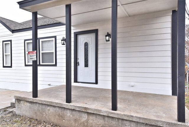 entrance to property with roof with shingles and a porch