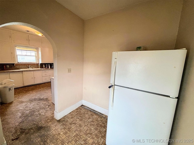 kitchen featuring white cabinets, a sink, arched walkways, freestanding refrigerator, and baseboards