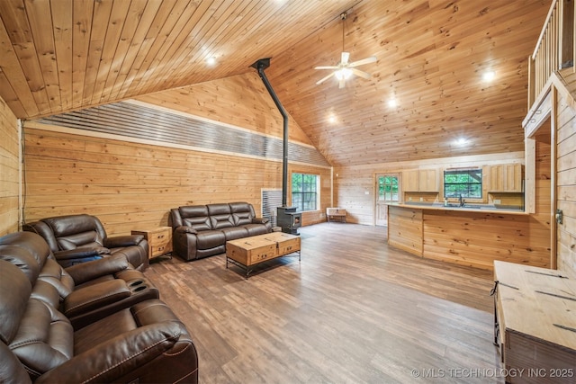 living room with a wood stove, high vaulted ceiling, wooden ceiling, wooden walls, and a ceiling fan