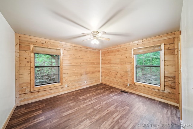 spare room featuring baseboards, wooden walls, dark wood finished floors, and ceiling fan
